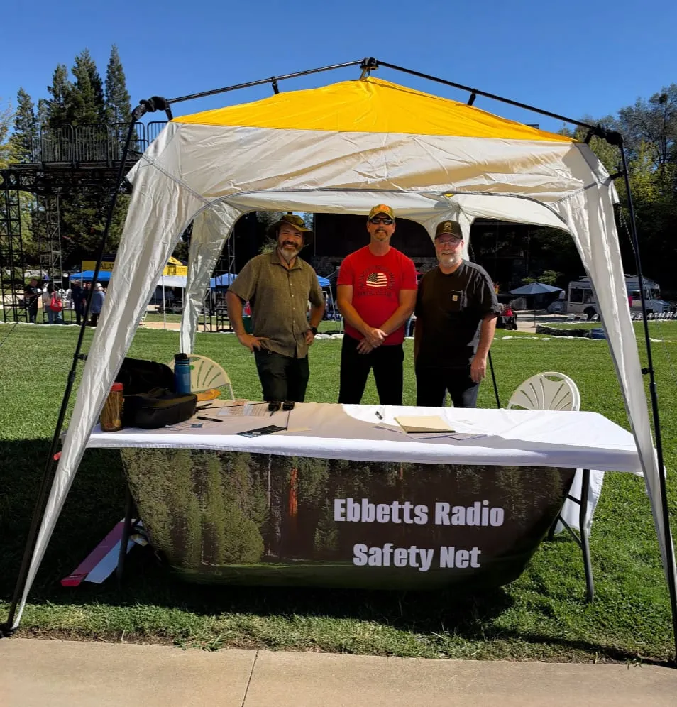 Alan, Dennis, and Mike standing under the ERSN canopy behind a table draped with an Ebbetts Radio Safety Net banner on the lawn at Ironstone Vineyards