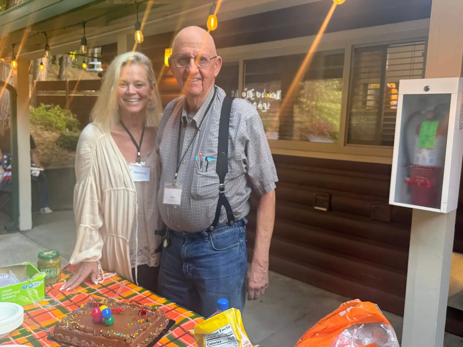 Ken and ERSN co-founder Marlaine smiling beside his chocolate birthday cake under the string lights on the lodge patio
